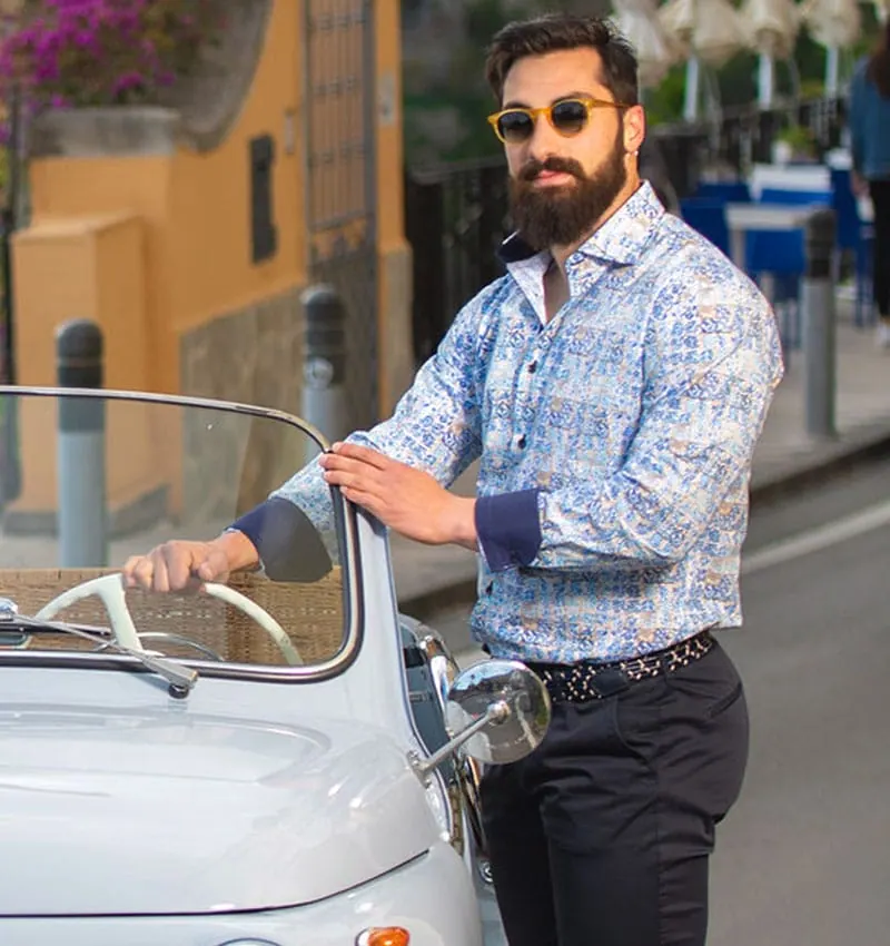 Un uomo con una camicia stampata azzurra, appoggiato a una vecchia auto bianca a Positano